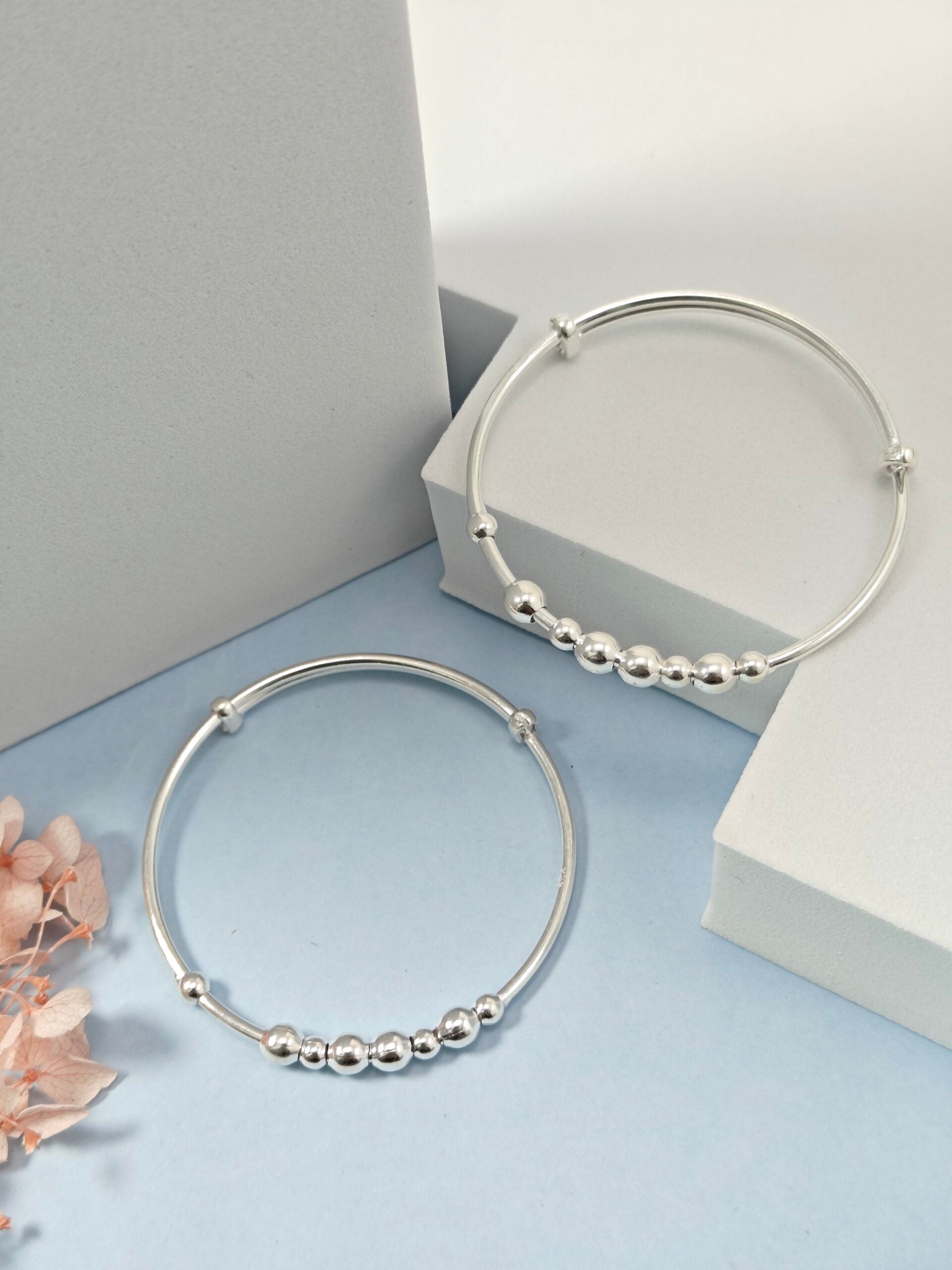 Silver hoop earrings with bead detailing on a light blue surface.